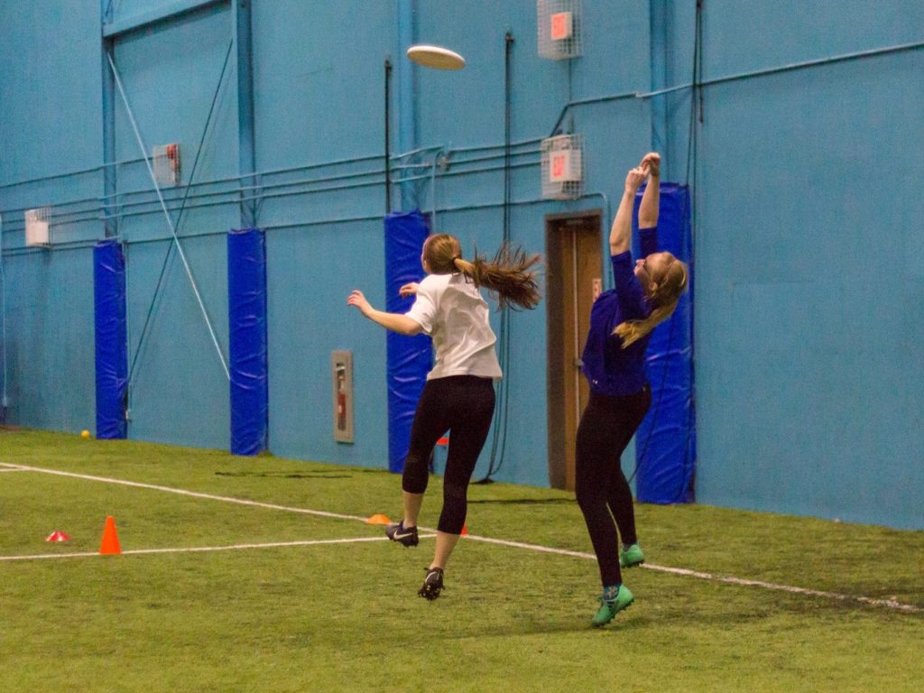 Two female-matching players jump for the disc in the St. John's Women's Ultimate Recreational League (SWURL).